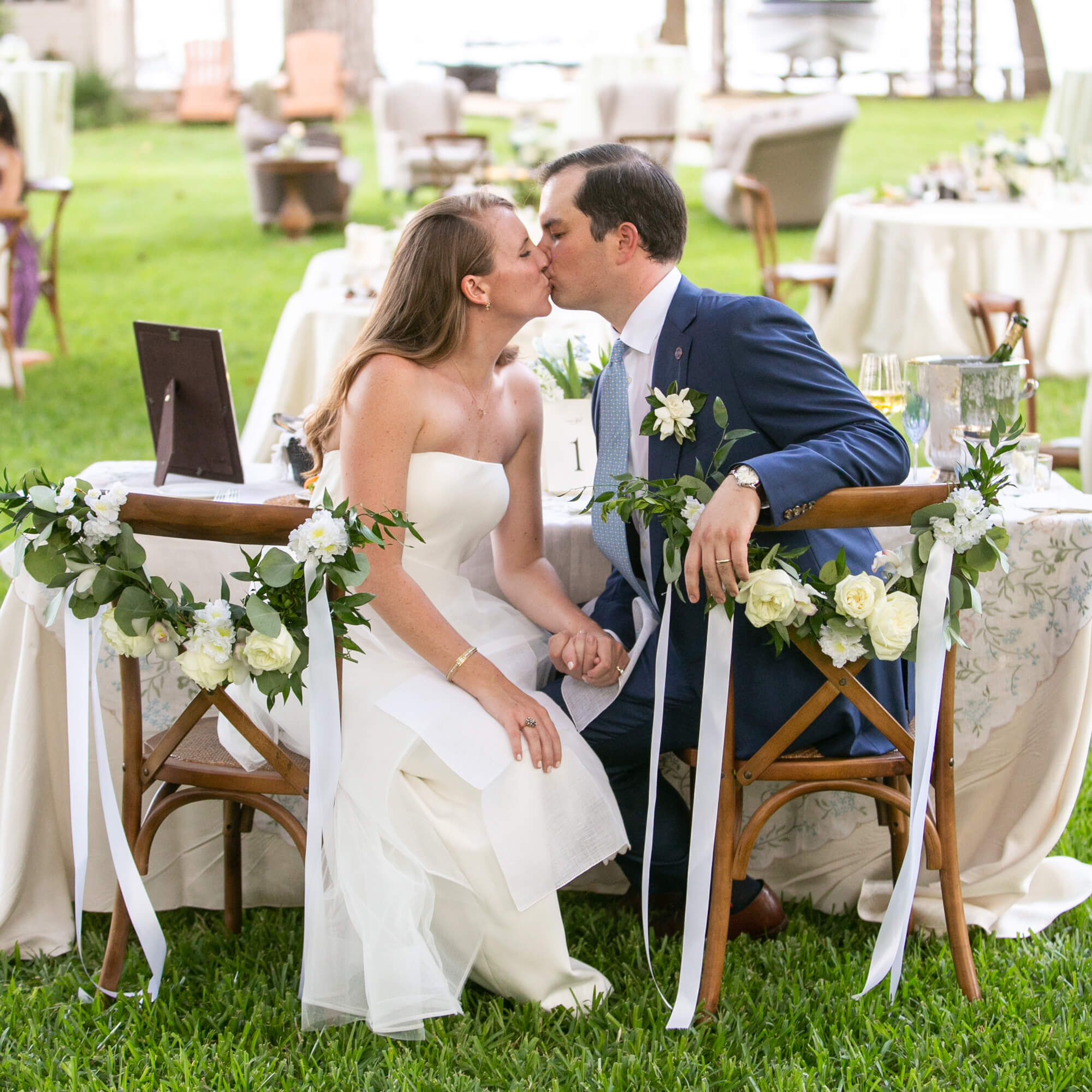 Bride and groom kissing at reception table outside