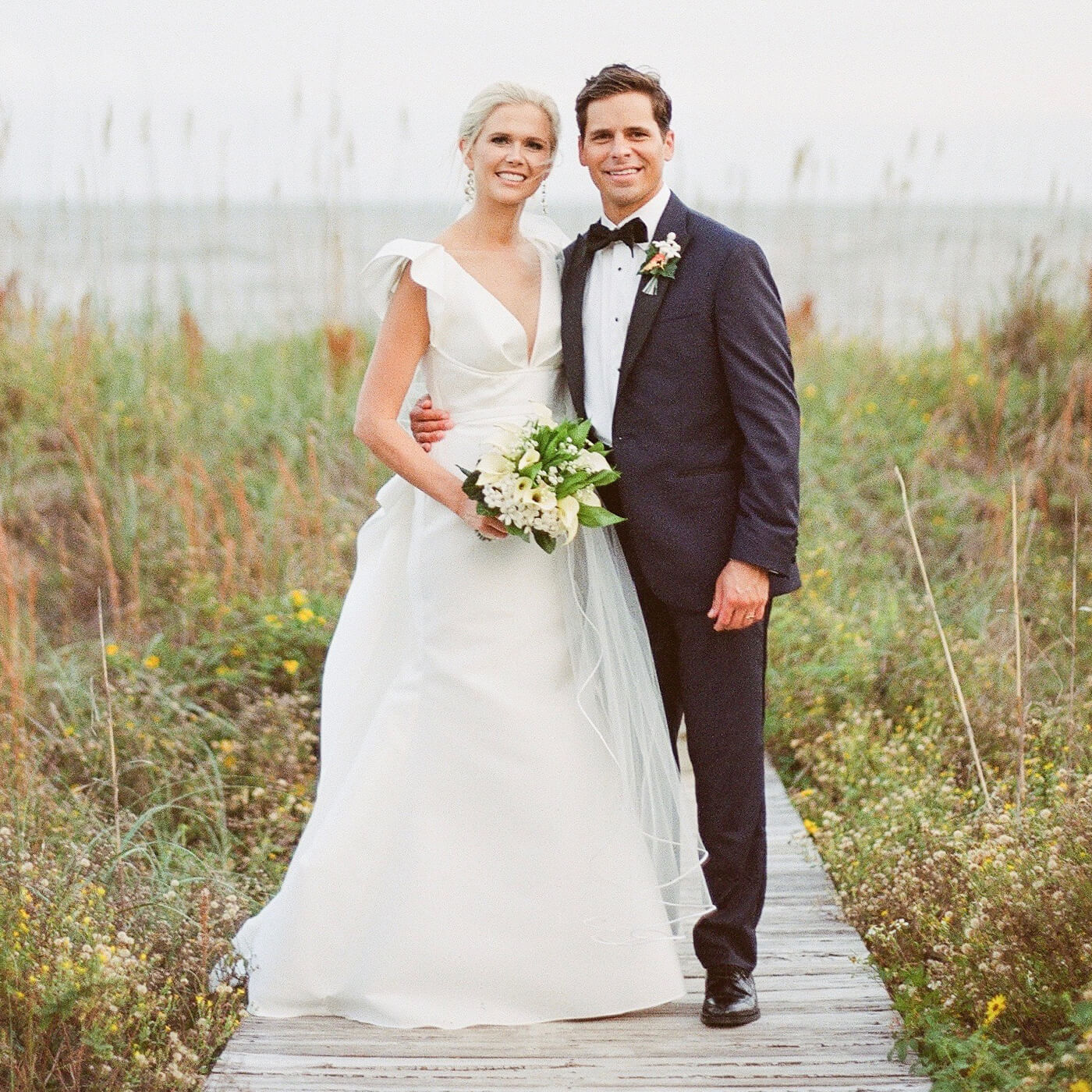 Bride and groom posing on a walkway in front of the ocean
