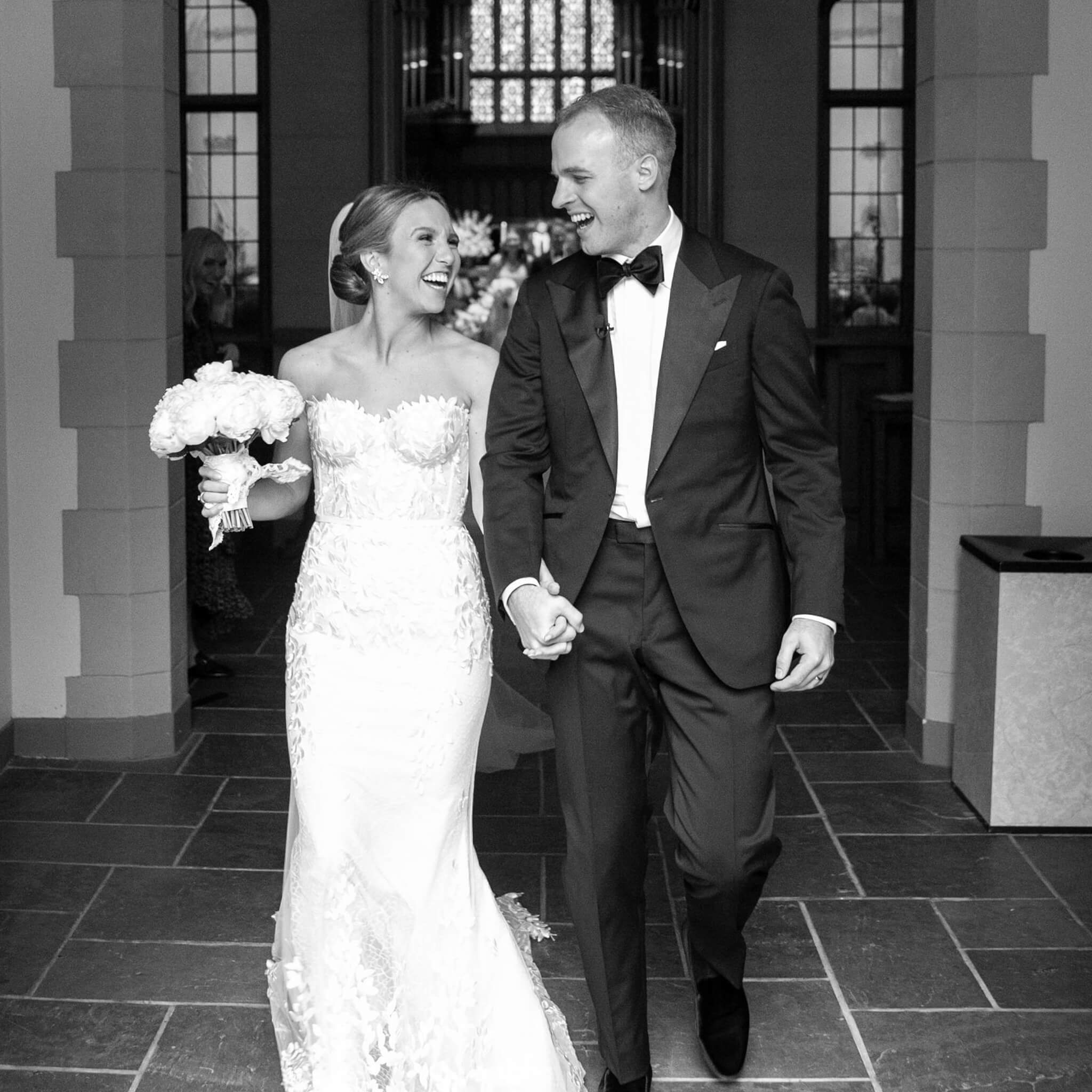 Black and white photo of bride and groom walking from ceremony